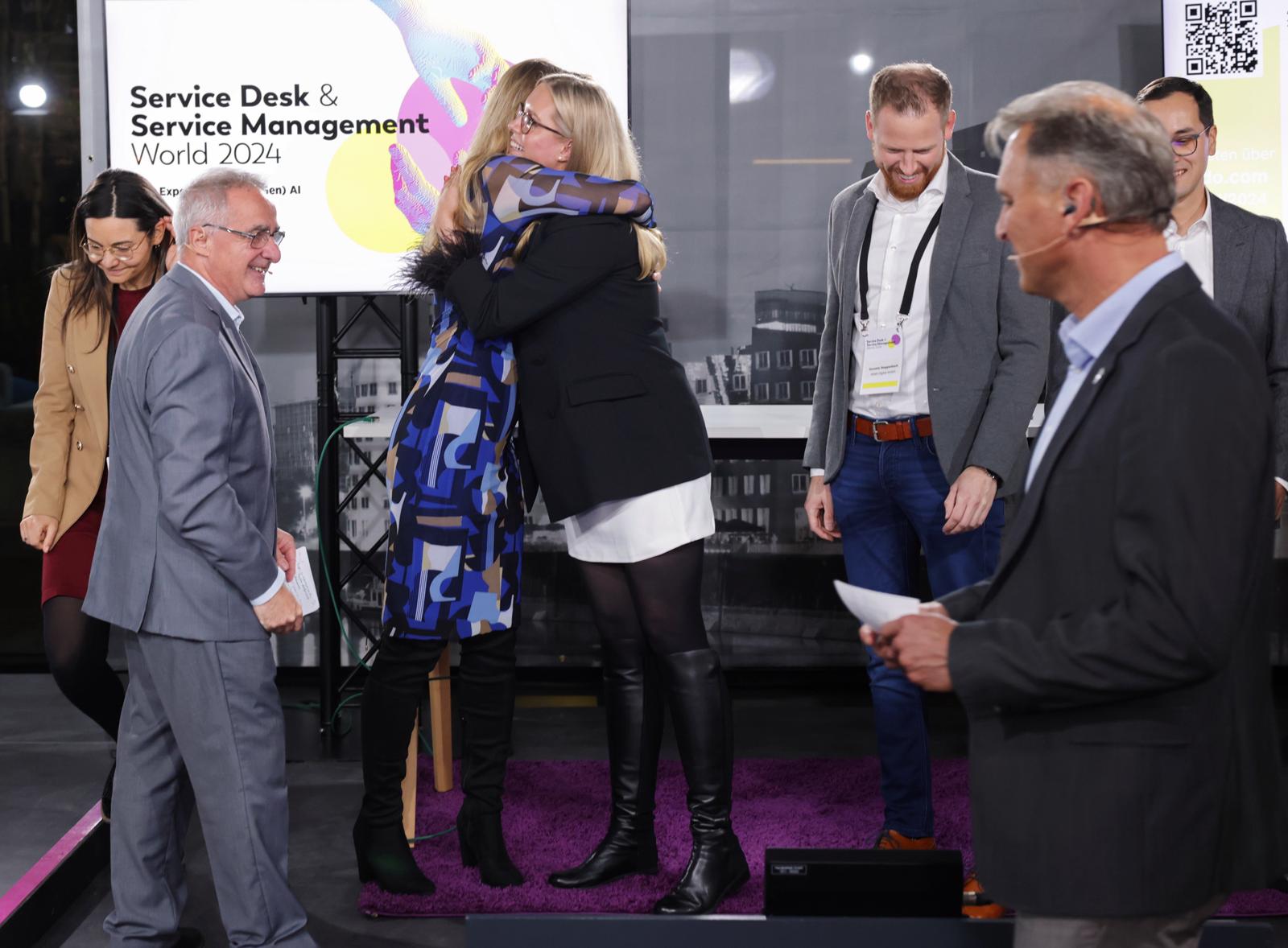Award recipients sharing a congratulatory hug during a company recognition ceremony