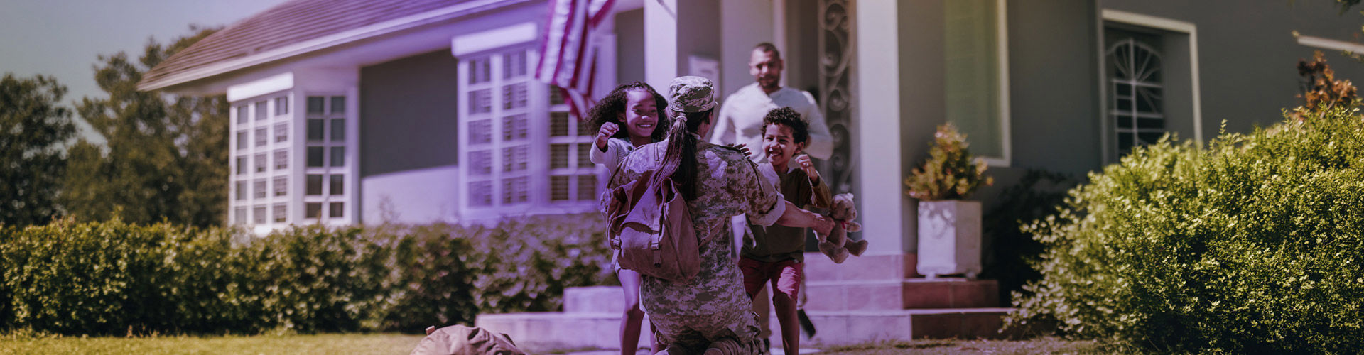 A U.S. military service member kneeling and embracing two joyful children running toward them outside a home.
