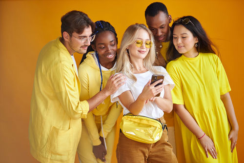 Group of diverse young people smiling and looking at a smartphone together against a yellow background