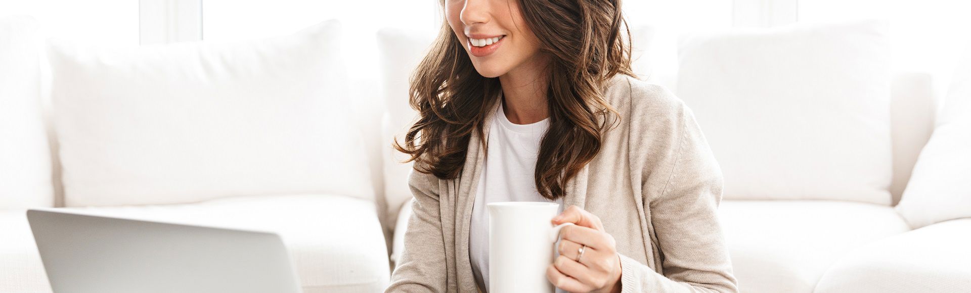 Woman smiling while using a laptop and holding a coffee mug at home.