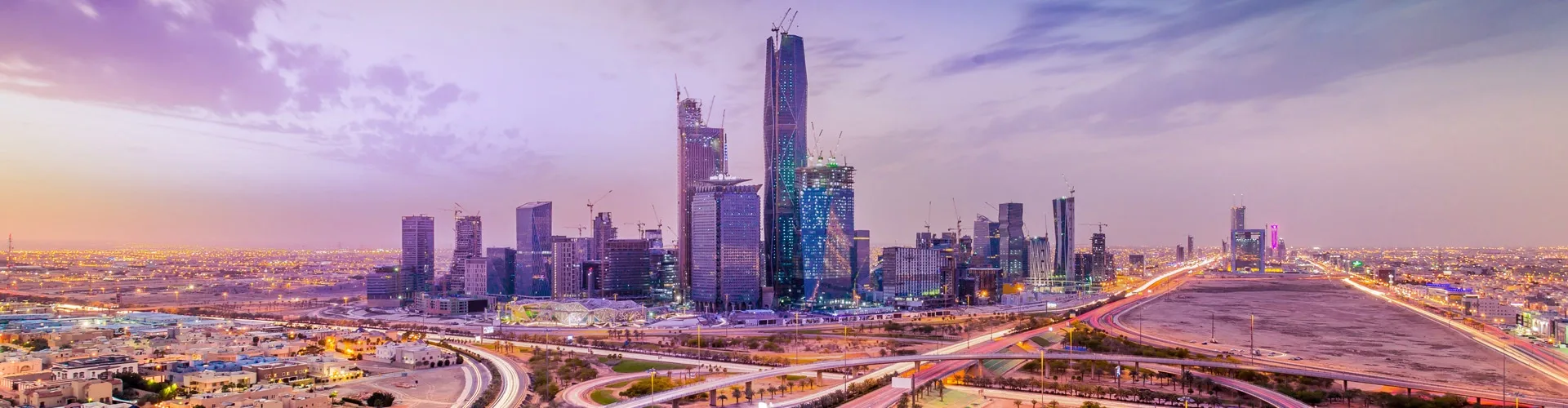 Skyscrapers stand prominently against a colorful sunset sky in a bustling cityscape, with intertwining highways and busy streets forming a vibrant urban environment.