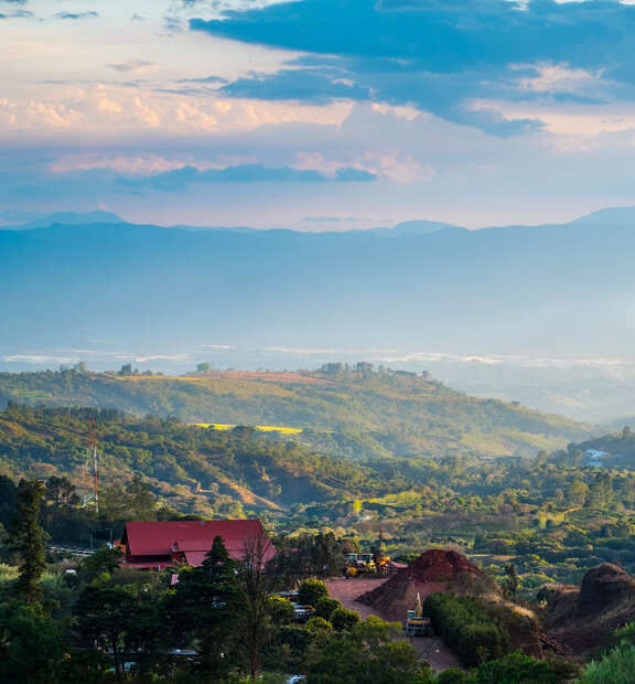 Distant rolling hills extend under a vast sky with scattered clouds, as red-roofed buildings nestle among trees in the lower foreground.