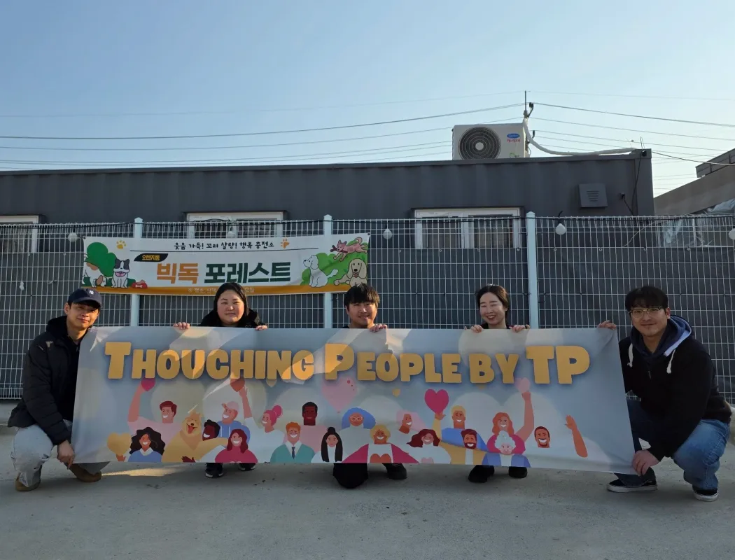 Five people hold a "Touching People by TP" banner at an outdoor volunteer event.