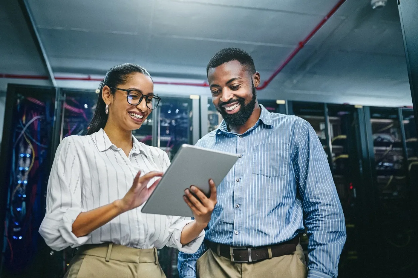 Two IT professionals reviewing information on a tablet in a server room.