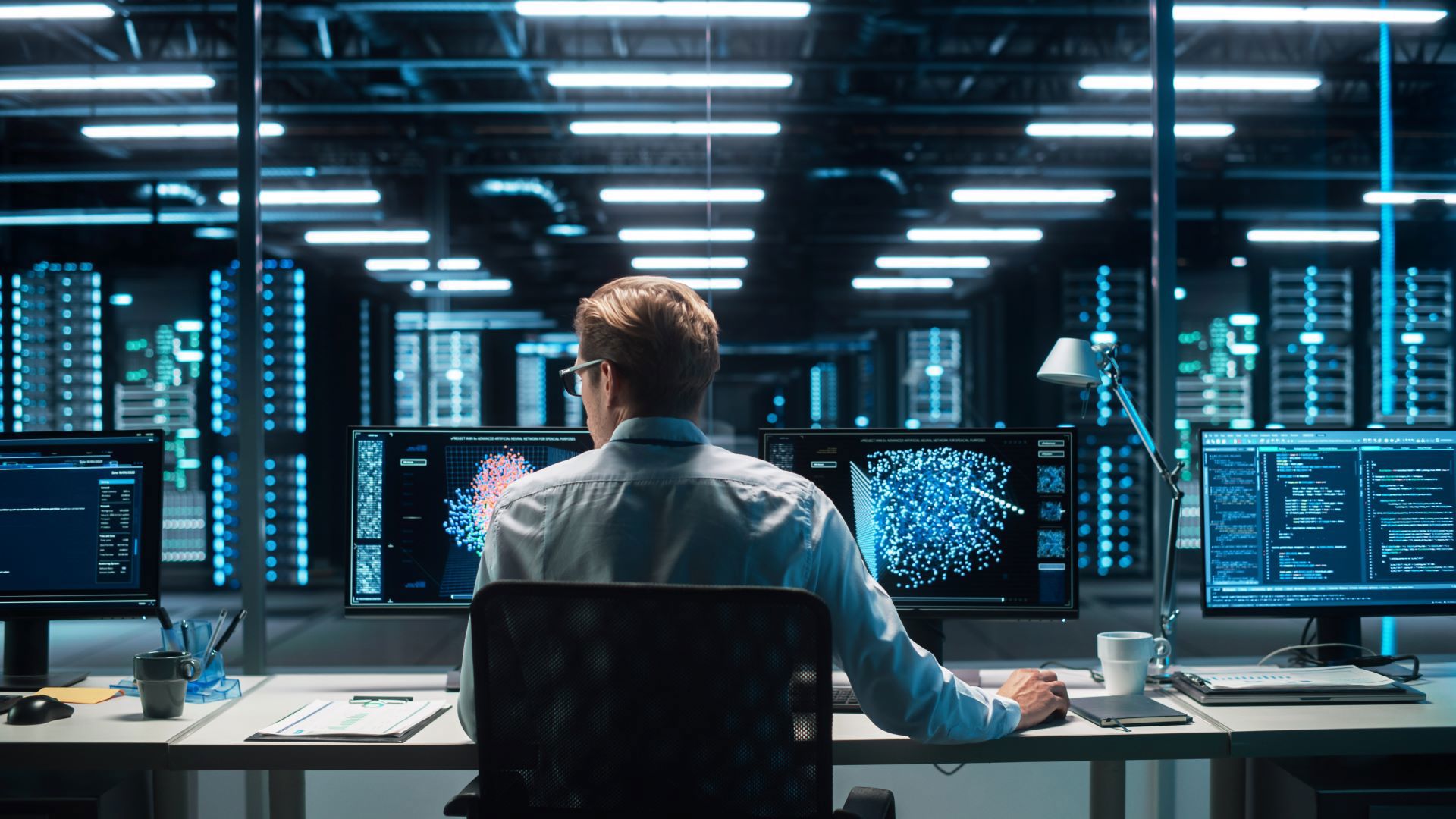 IT specialist monitoring data visualizations and code on multiple screens in a modern data center.
