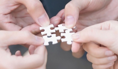 Several hands fit puzzle pieces together to symbolize business cooperation.