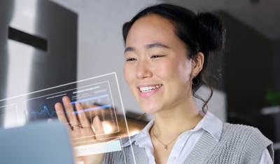 Asian woman working on a computer, interacting with futuristic 3D elements emerging from the screen, representing Human CX innovation.