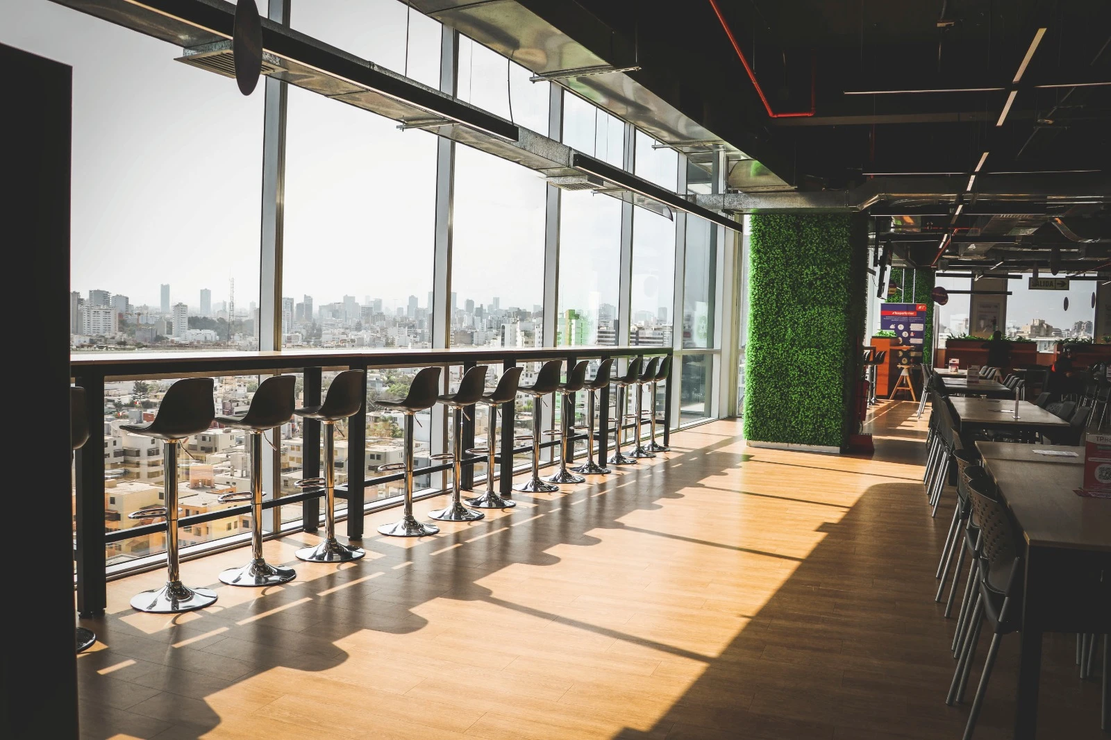 TP Magdalena cafeteria with high stools facing city skyline through large windows.