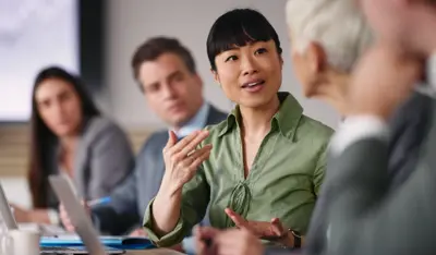 Asian businesswoman leading a meeting with colleagues at a conference table.