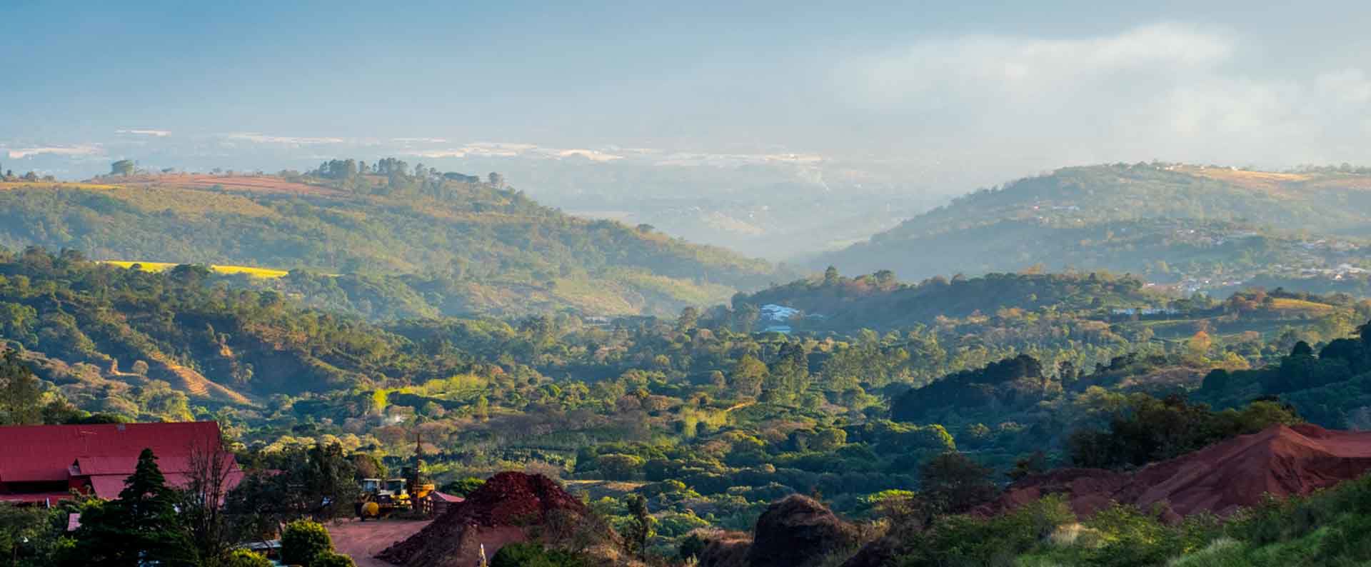 Lush green hills and valleys with scattered houses and distant mountains under a clear sky.