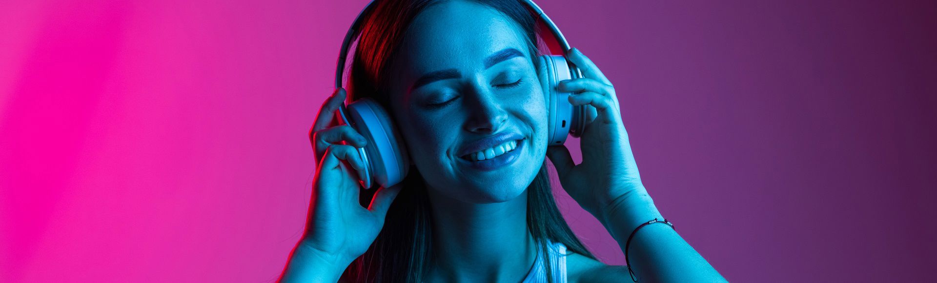 Woman smiling while listening to music with headphones against a colorful background.