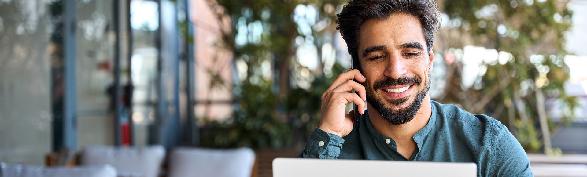 Smiling man on the phone while working on his laptop outdoors. 