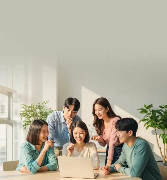 A diverse team of young professionals collaborates and discusses ideas around a laptop in a bright office
