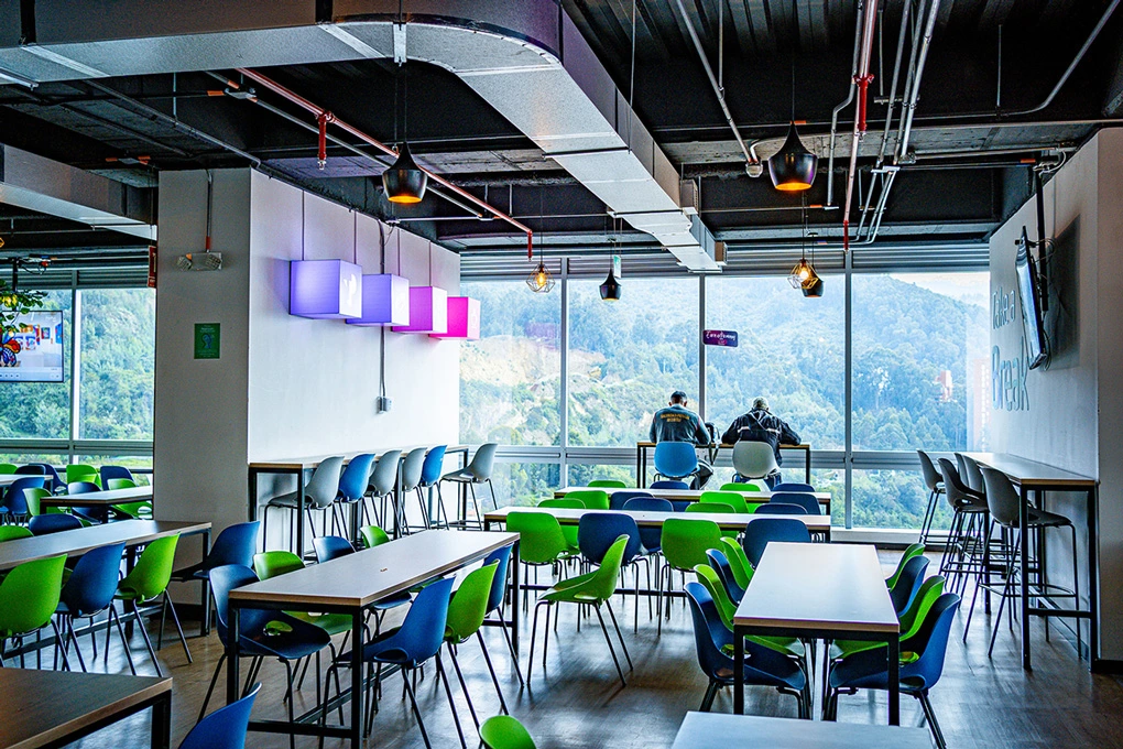 TP cafeteria with colorful chairs and mountain view through large windows.