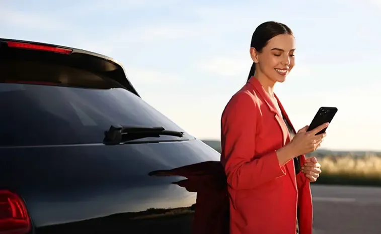Woman holding a phone in front of her parked car while waiting for assistance.