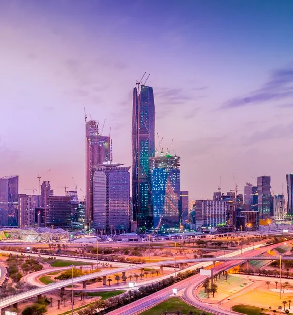 Skyscrapers stand prominently against a colorful sunset sky in a bustling cityscape, with intertwining highways and busy streets forming a vibrant urban environment.
