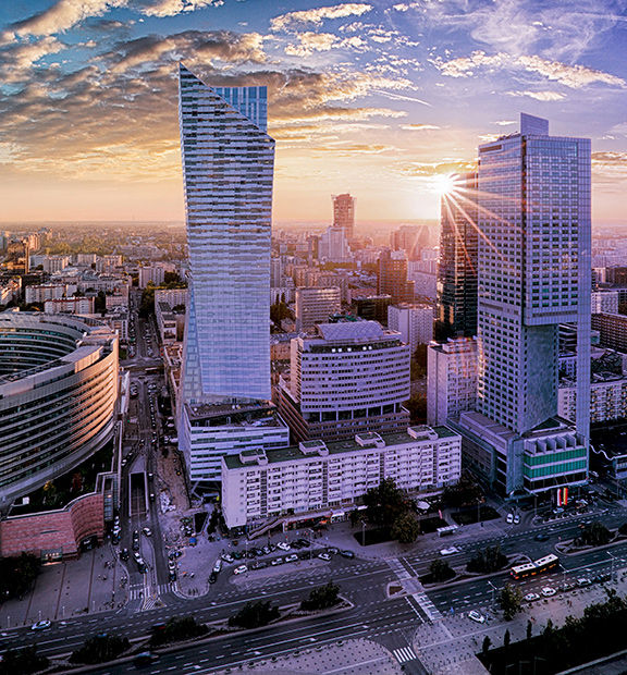 Panoramic aerial view of Warsaw, Poland, at sunset, featuring modern skyscrapers, busy streets, and the city skyline.