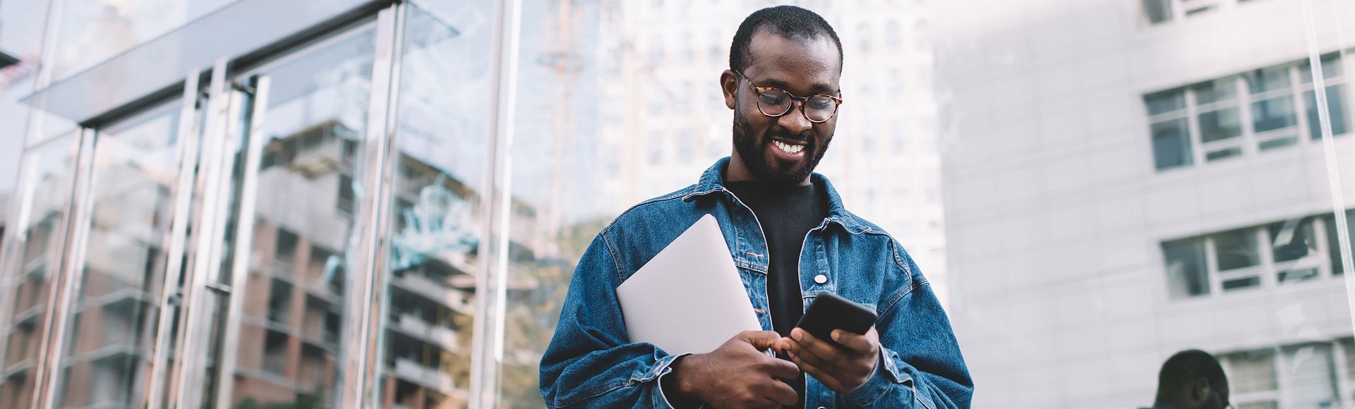 A smiling Afro-descendant man looks at his phone, highlighting the human edge in tech.