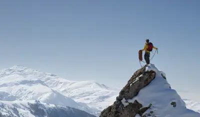 Mountaineer standing on a snowy peak above a mountain range.