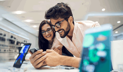 Smiling couple with glasses choosing a smartphone in a modern electronics store.