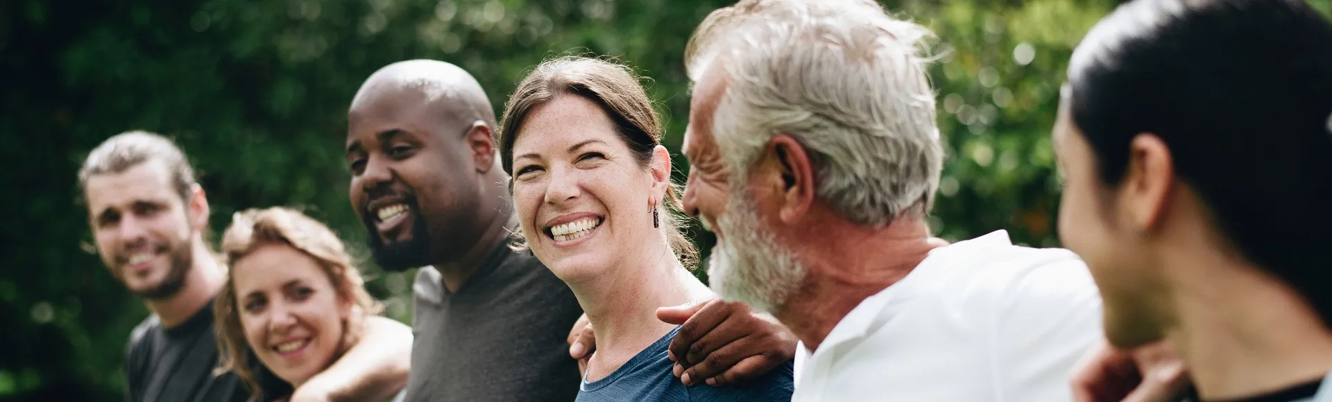 Group of people smiling outdoors with arms around each other.