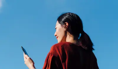 Woman using a smartphone outdoors under a clear blue sky.