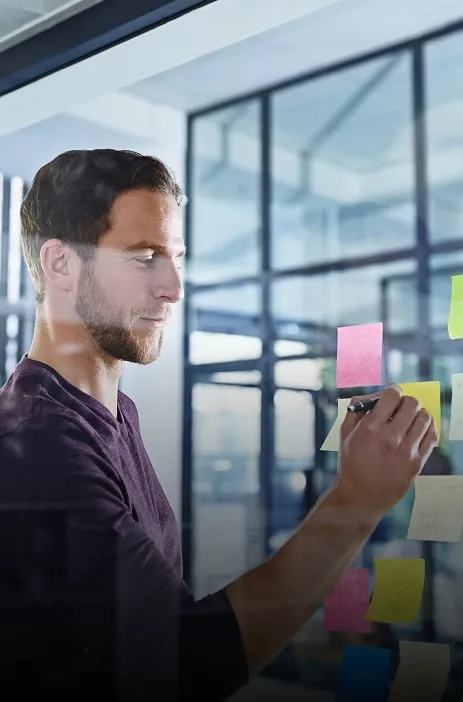 TP employee writing on a glass board with colorful sticky notes in an office setting.