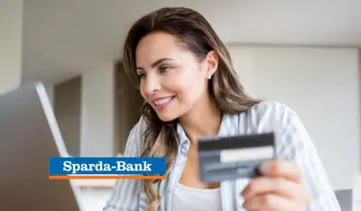 Woman using a computer while holding a card, representing banking services.