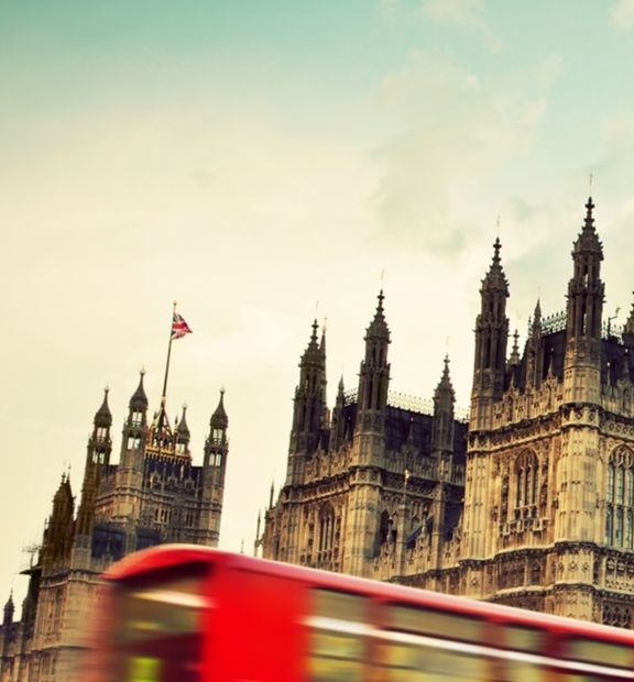Red double decker bus passing by Palace of Westminster in London.