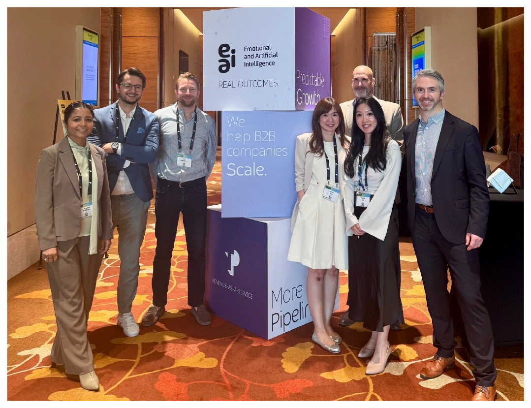 A diverse team poses at a conference booth promoting B2B growth solutions.
