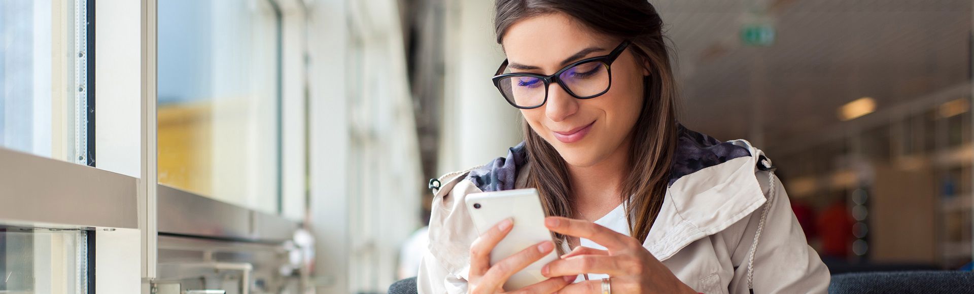 Woman wearing glasses using a smartphone while seated indoors.