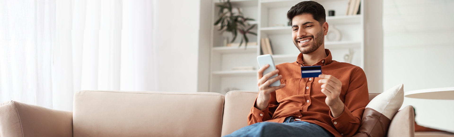 TP customer smiling while making a mobile payment with a credit card at home.