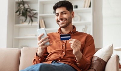 TP customer smiling while making a mobile payment with a credit card at home.