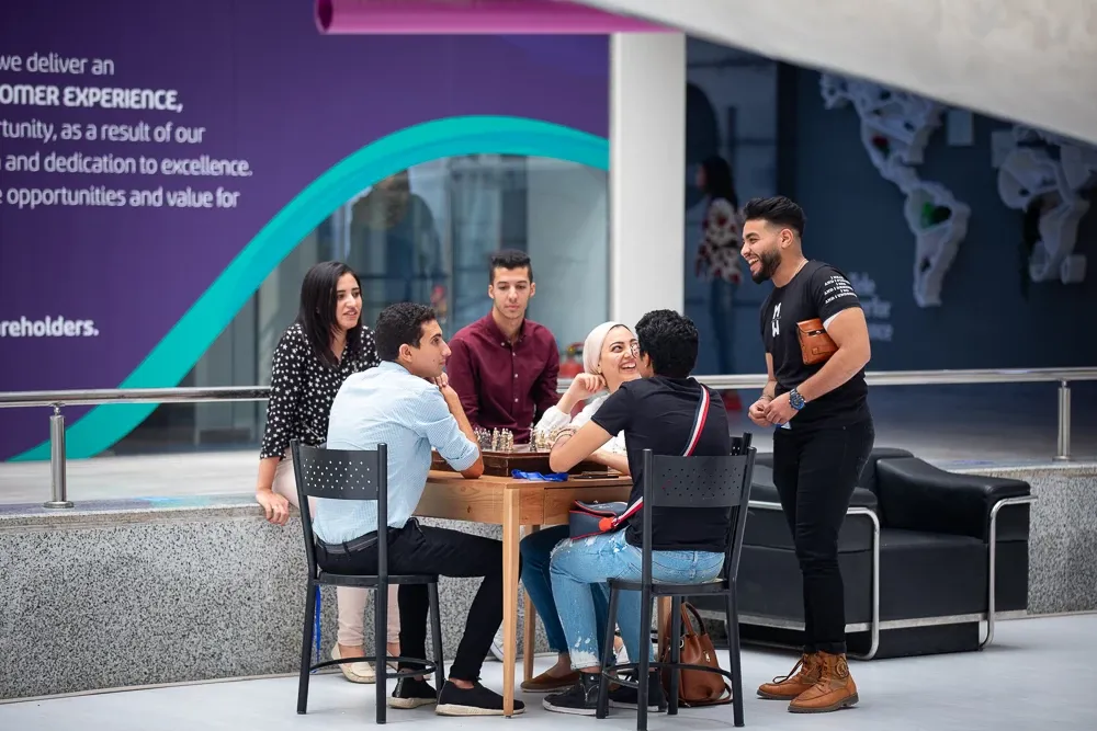 Group of young professionals smiling and talking around a table in a modern Teleperformance office.