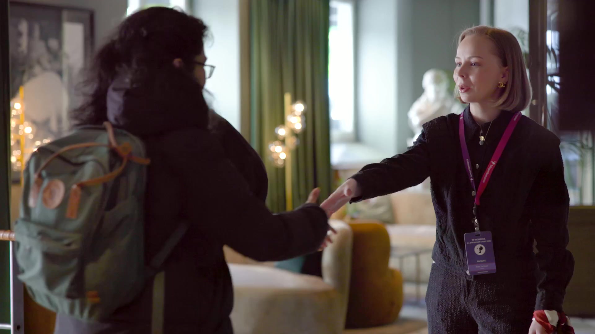 Woman with event badge greeting another person with handshake indoors