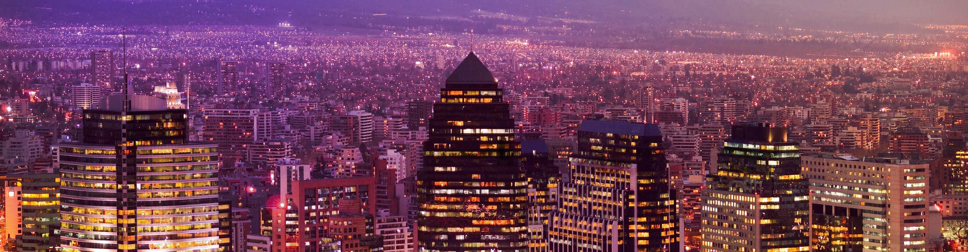 Panoramic nighttime view of Santiago, Chile, with illuminated skyscrapers and a dense cityscape stretching toward the horizon.