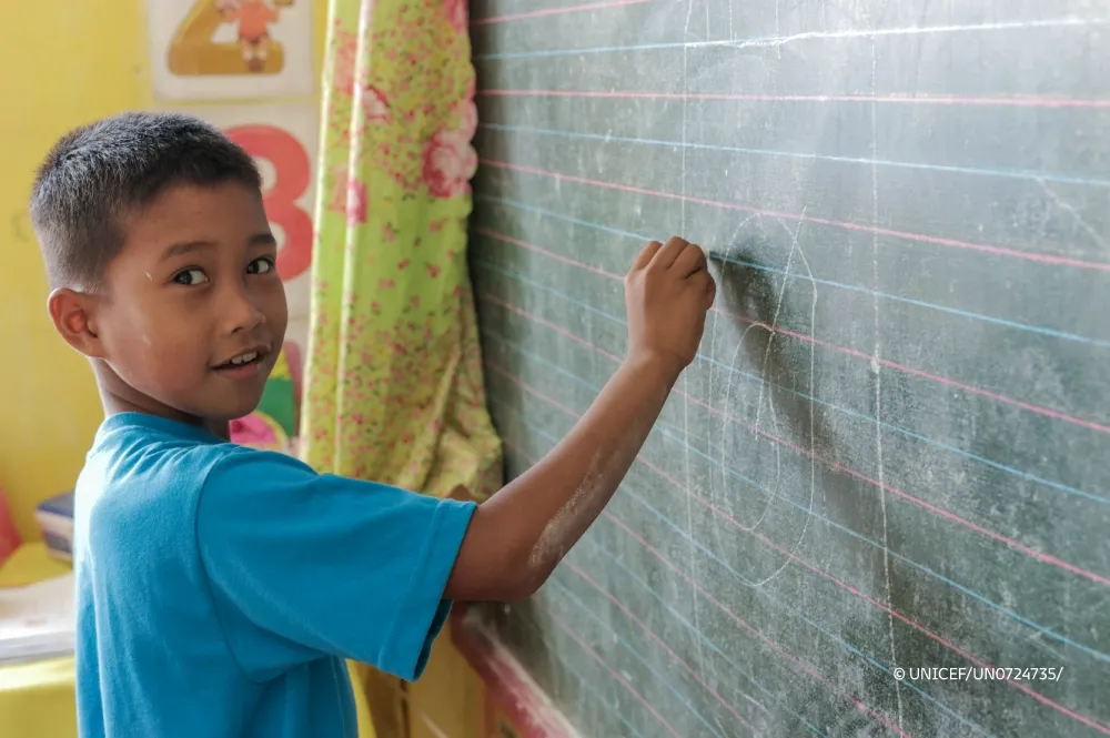 Student writes on a chalkboard in a classroom.