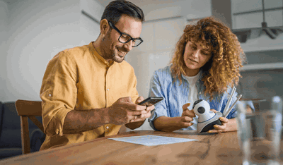 Couple at a table reviewing a phone and security camera, illustrating AI-powered insights.