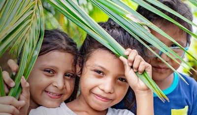 Smiling children behind palm leaves, symbolizing protection in TP for UNICEF programs.