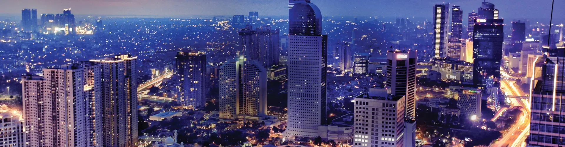 Jakarta cityscape at night with illuminated skyscrapers and busy roads.