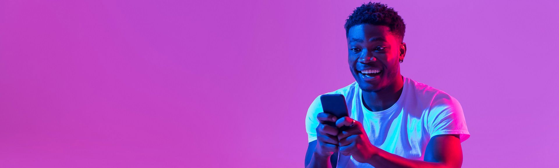 Smiling man holding a smartphone against a bright pink background.