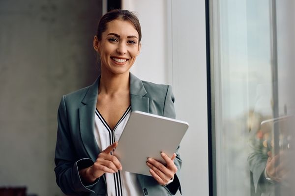 Smiling professional holding a tablet by a window in a modern office.