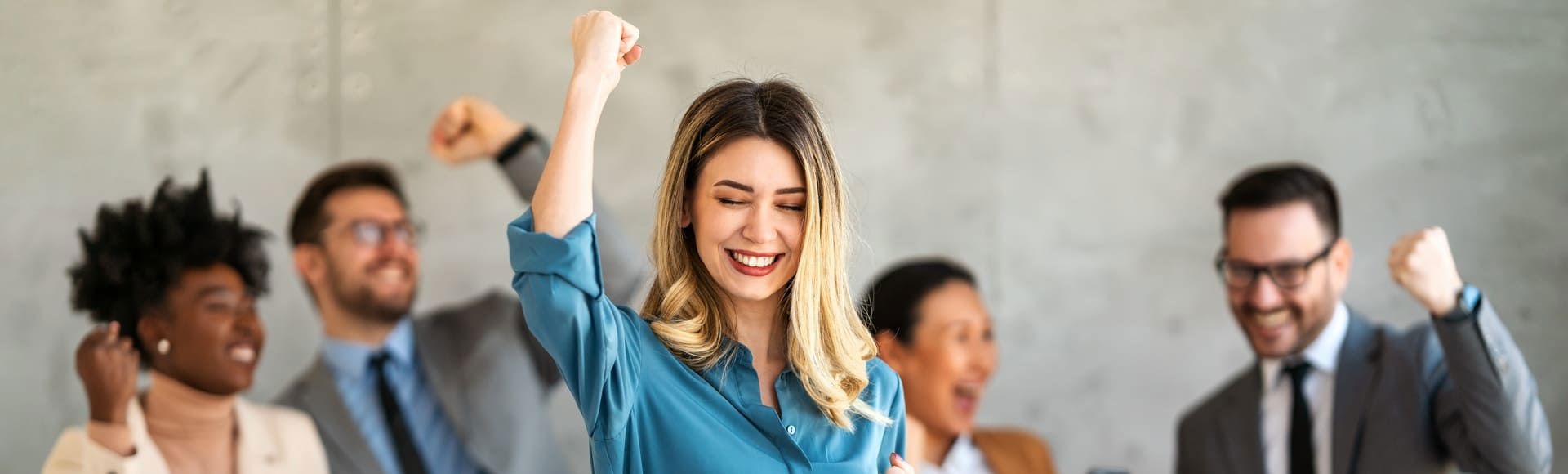 Team celebrating success with a smiling woman raising her fist in the foreground.