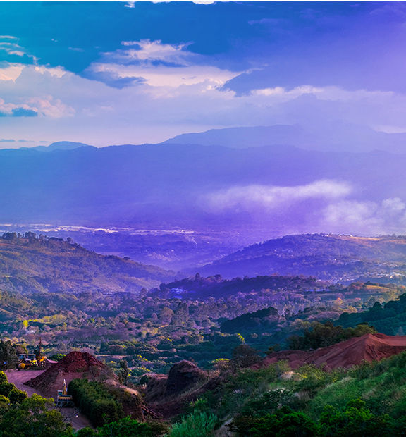 Panoramic view of Costa Rica’s lush mountainous landscape, with rolling green hills, dense vegetation, agricultural fields, and misty valleys beneath a cloudy sky.
