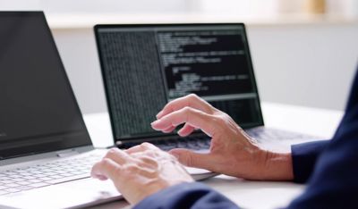 Person coding on two laptops, representing TP’s work with Agentic AI and advanced tech.