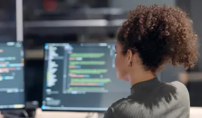 TP team reviewing code on multiple monitors in a collaborative workspace.