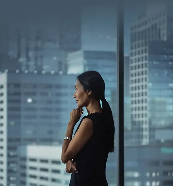 Thoughtful Asian businesswoman looking out the window of her modern office.