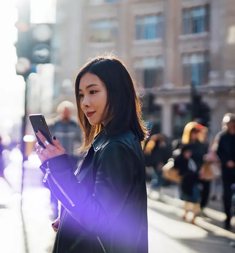 Woman using a smartphone on a city street, representing TP’s smartshoring services.