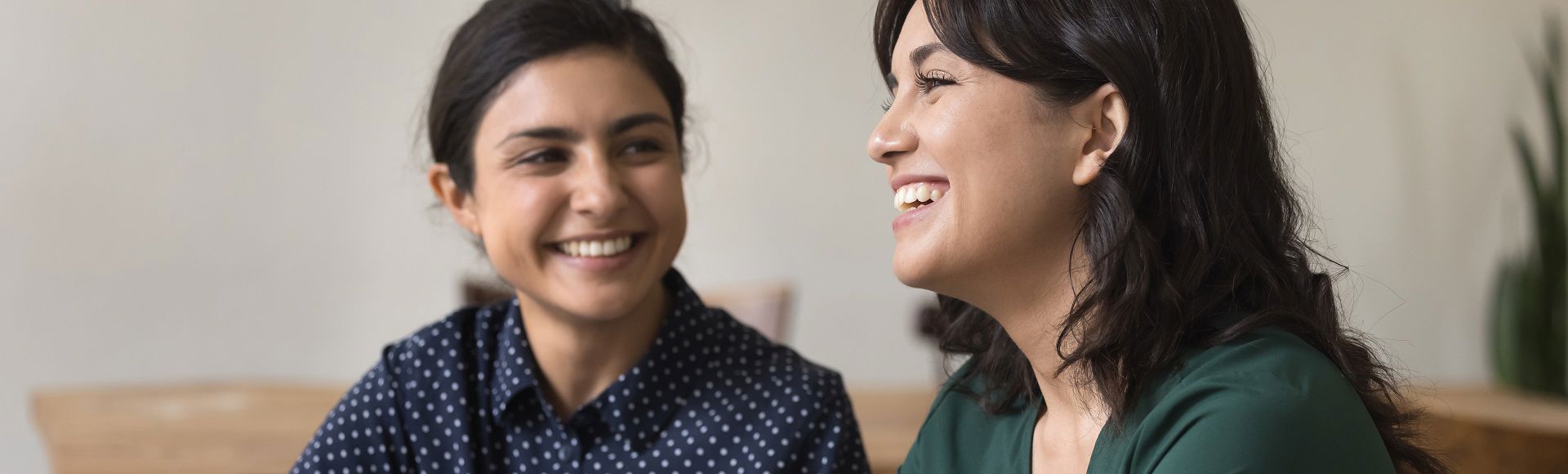 Two women smiling and talking together in a casual indoor setting.