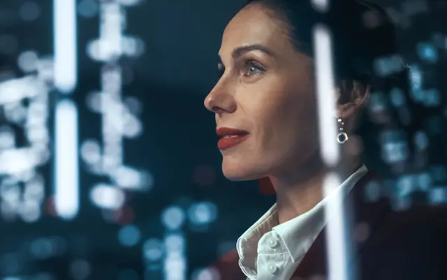 Thoughtful businesswoman observing a brightly lit city skyline at night.